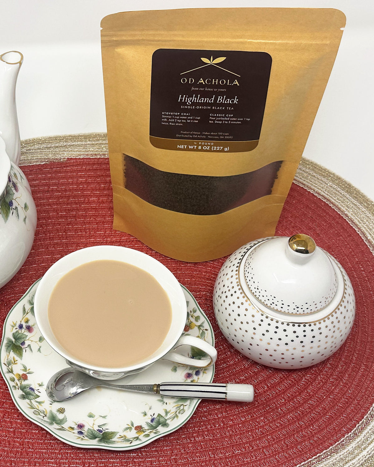 Cup of Kenyan milk chai with a floral teapot, sugar bowl and a pouch of Highland Black tea