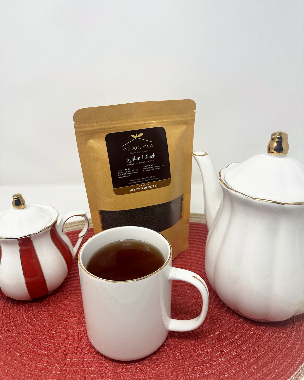 Mug of brewed Highland Black tea with a white teapot, creamer and the Od Achola pouch