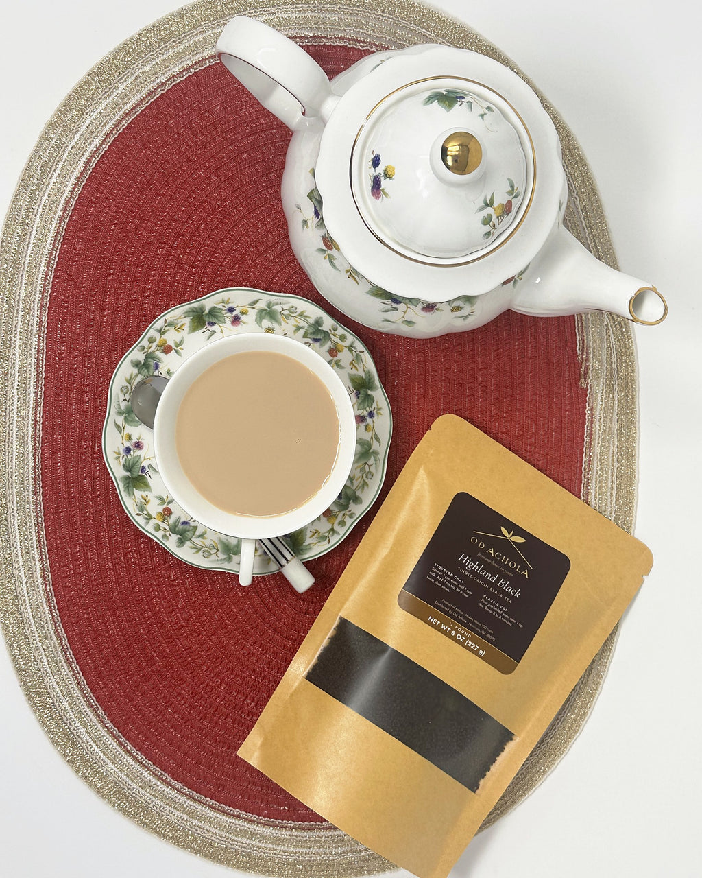 Overhead view of a cup of chai, a floral teapot and a pouch of Od Achola Highland Black tea
