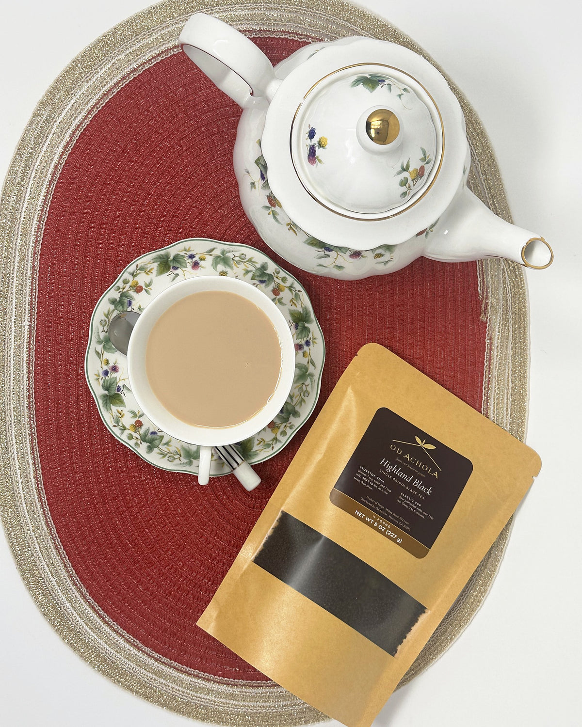 Overhead view of a cup of chai, a floral teapot and a pouch of Od Achola Highland Black tea